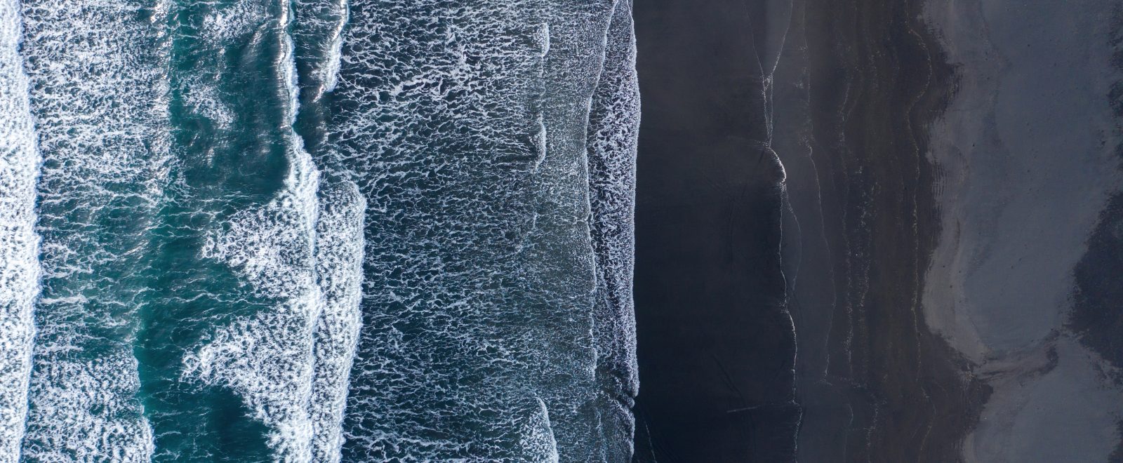 Aerial view of Atlantic ocean waves washing black sandy beach