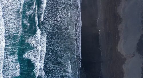 Aerial view of Atlantic ocean waves washing black sandy beach