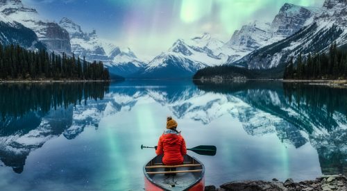 Beautiful aurora borealis over spirit island with female traveler on canoe at Jasper national park