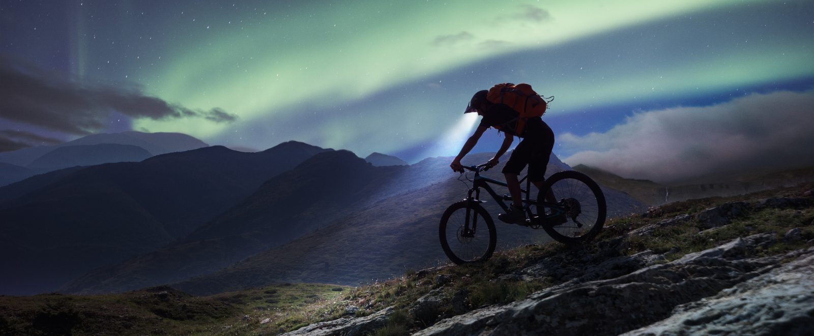 Mountain biker riding in mountain under aurora Polaris.