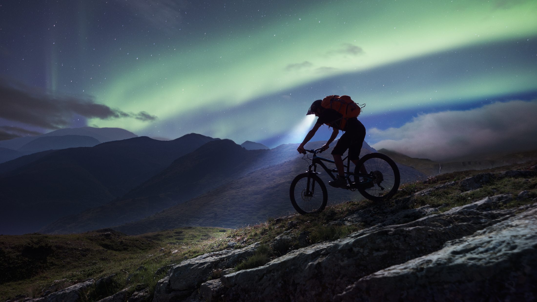 Mountain biker riding in mountain under aurora Polaris.