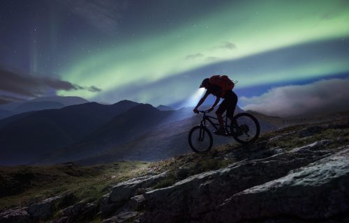 Mountain biker riding in mountain under aurora Polaris.