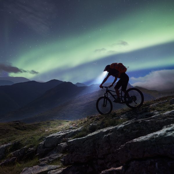 Mountain biker riding in mountain under aurora Polaris.