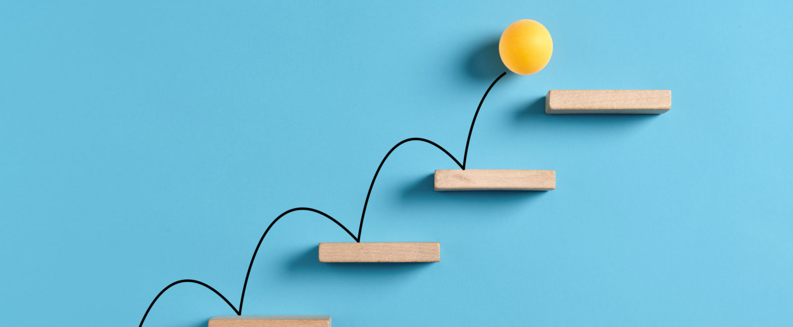 Yellow ball bouncing up wooden stairs in front of a blue background