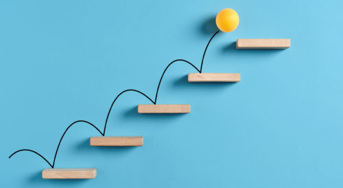 Yellow ball bouncing up wooden stairs in front of a blue background