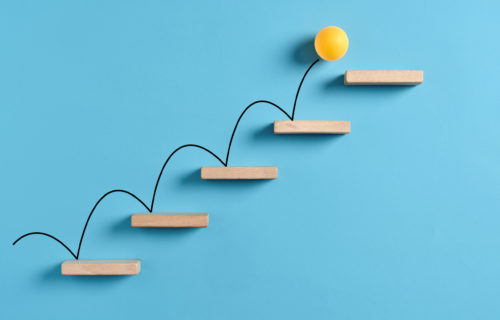 Yellow ball bouncing up wooden stairs in front of a blue background