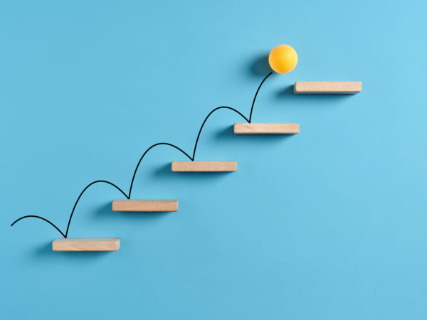 Yellow ball bouncing up wooden stairs in front of a blue background