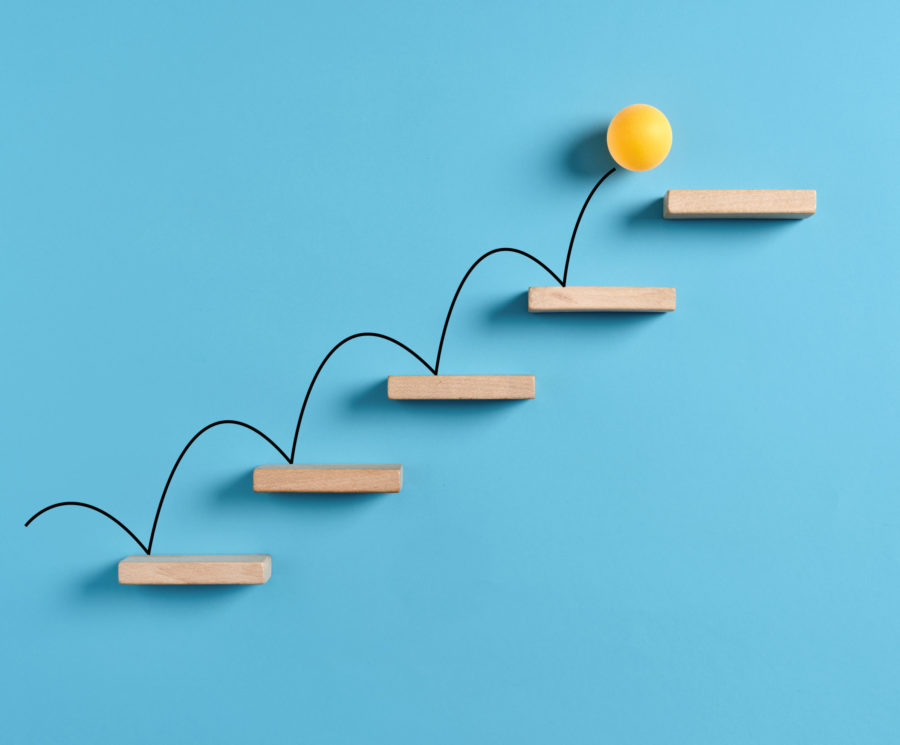 Yellow ball bouncing up wooden stairs in front of a blue background