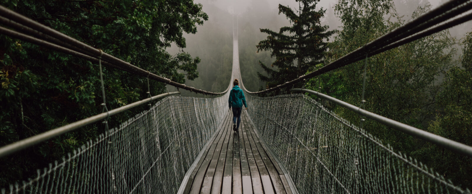 Lady walking over a rope and wood bridge in stormy weather