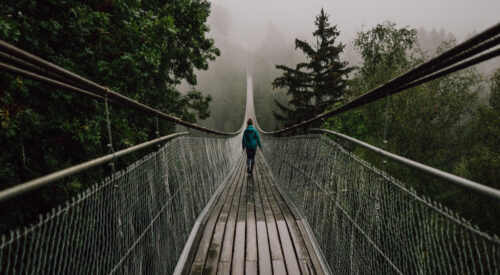 Lady walking over a rope and wood bridge in stormy weather