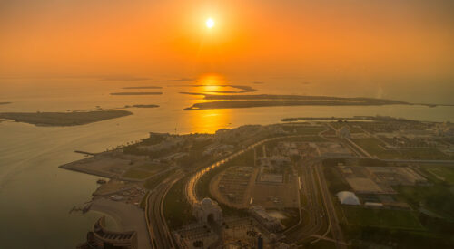 Aerial view of Abu Dhabi, UAE, including Qasr Al Watan and the Corniche. Coastal urban development meets the Persian Gulf during sunset glow.