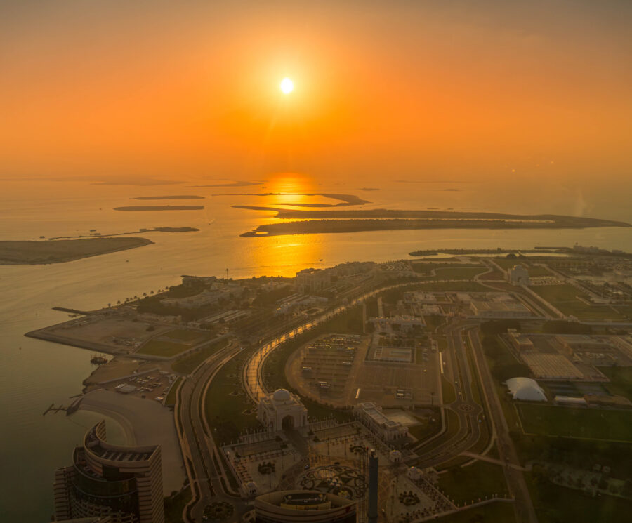 Aerial view of Abu Dhabi, UAE, including Qasr Al Watan and the Corniche. Coastal urban development meets the Persian Gulf during sunset glow.